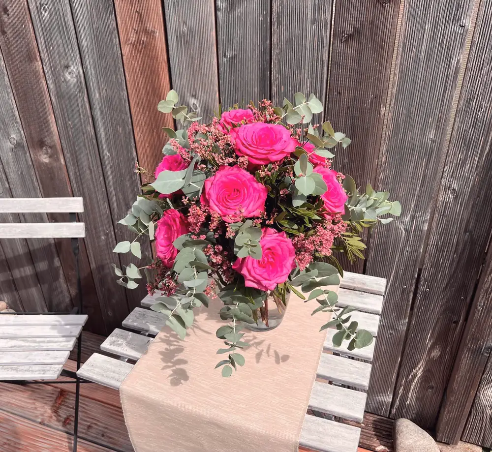 Blumenstrauss mit pinken Rosen auf einem Gartentisch