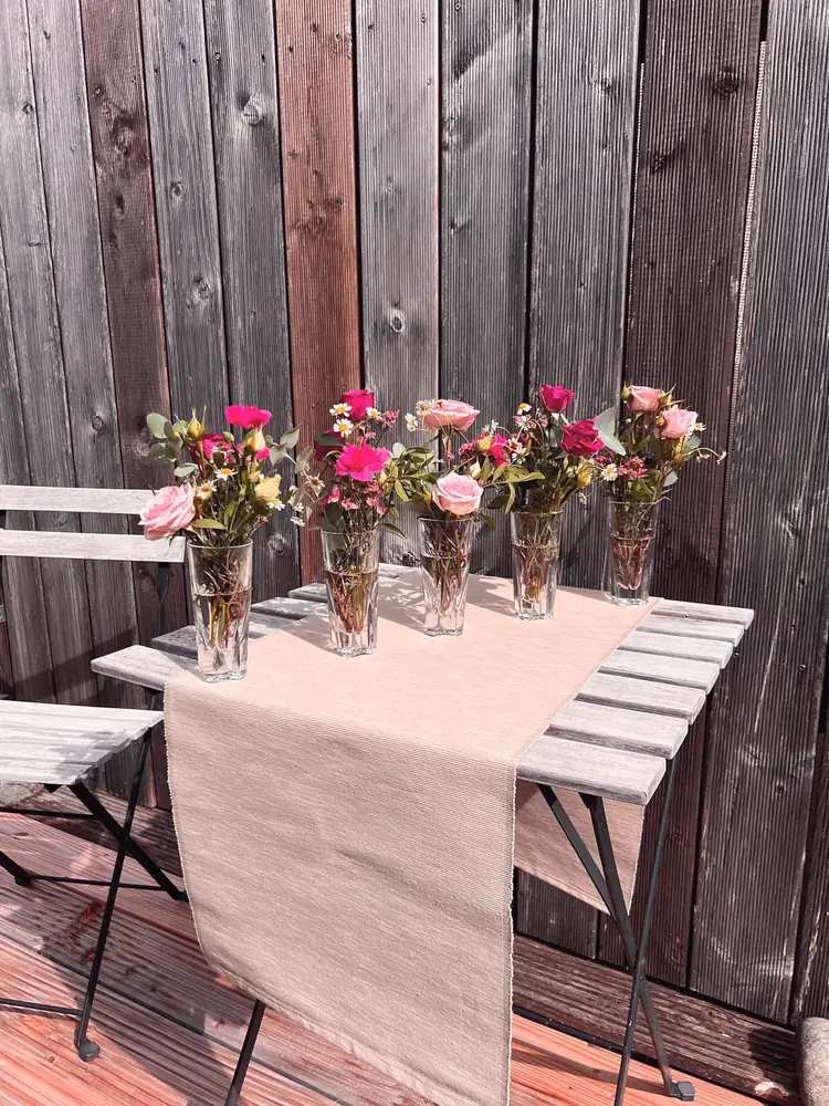 Kleine Vasen mit rosa Blumen auf einem Tischläufer
