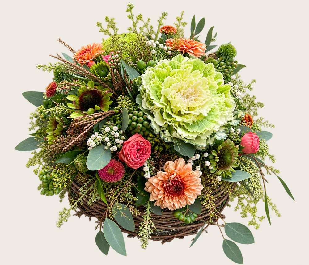 Gesteck mit Zierkohl und Rosen im Weidenkorb
