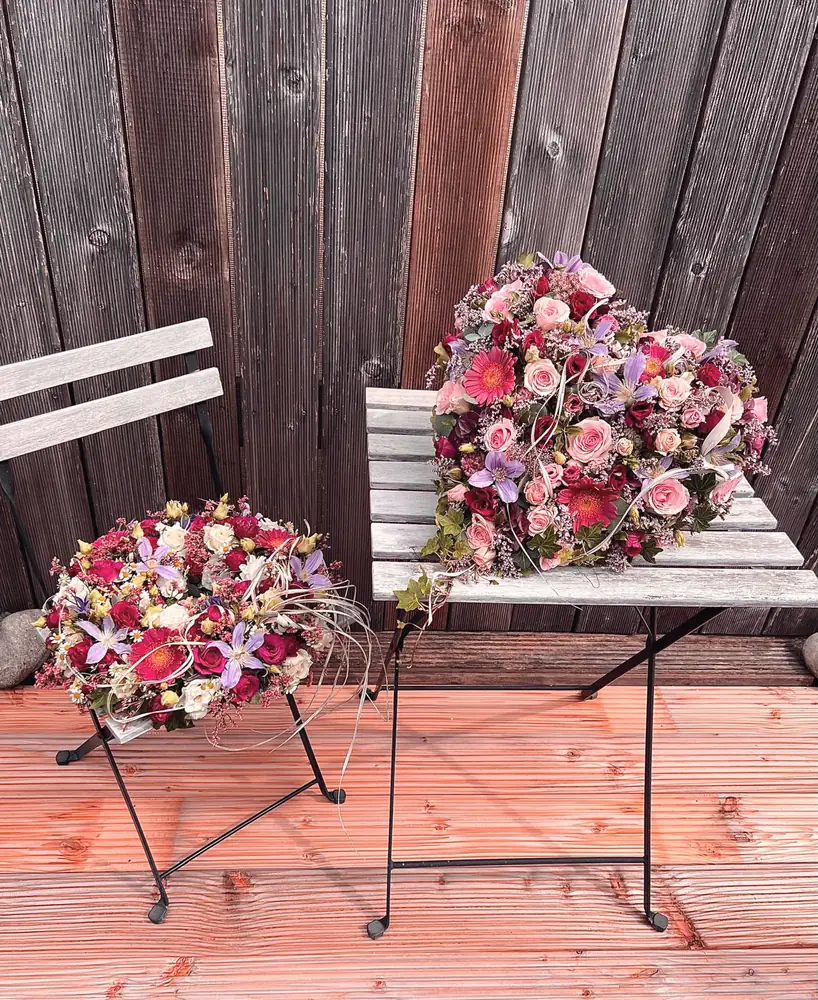 Zwei Trauerkränze in Rosa und Violett auf Gartenstuhl und Tisch