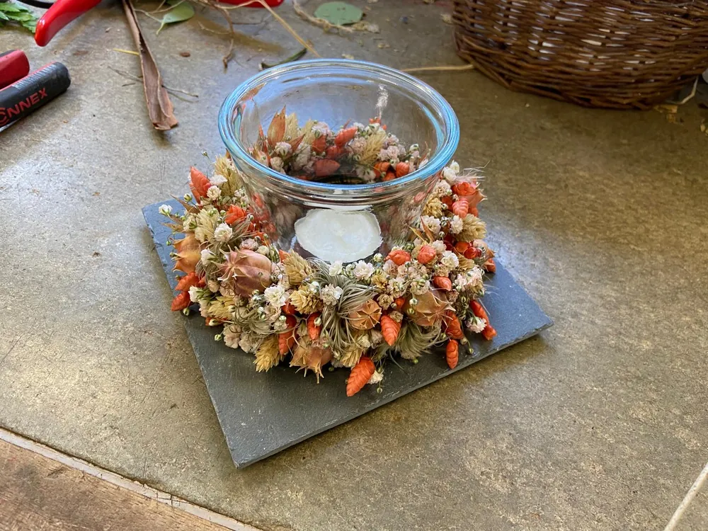 Windlicht mit Kranz aus Trockenblumen in Orange auf Schieferplatte